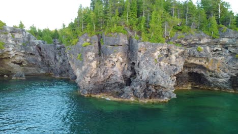 Cinematic-flight-over-rocky-coast-of-Georgian-Bay-with-turquoise-lake-and-dense-forest-in-Ontario,-Canada
