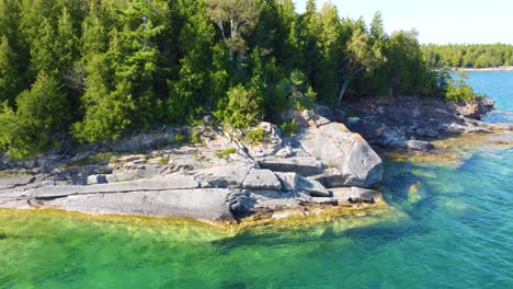 Flying-over-rocky-coast-of-Georgian-Bay-with-turquoise-lake-and-dense-forest-in-Ontario,-Canada