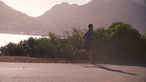 Young-man-running-on-an-empty-coastal-road,-slow-motion