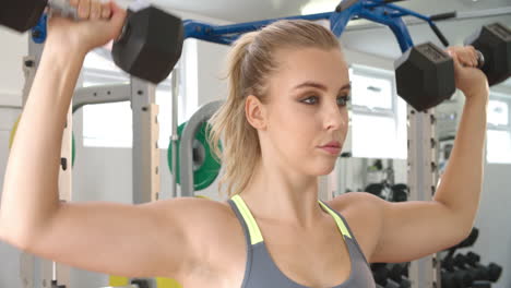Young-woman-shoulder-pressing-dumbbells-at-a-gym