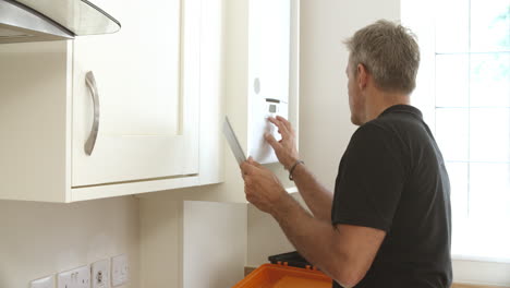 Middle-aged-technician-with-digital-tablet-servicing-boiler