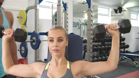 Young-woman-lifting-dumbbells-with-trainer-at-a-gym