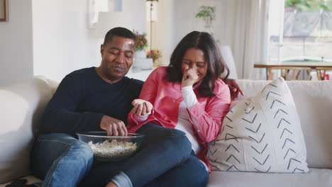 Happy-African-American-couple-reclining-on-sofa,-watching-TV-and-eating-popcorn,-close-up