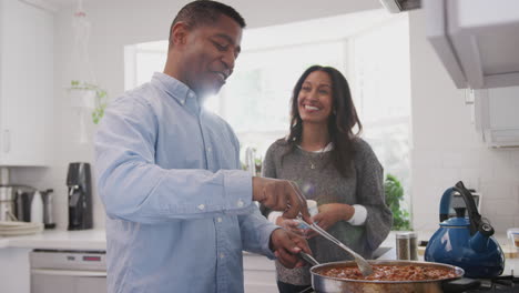 Middle-aged-African-American-couple-stand-talking-in-the-kitchen,-man-preparing-food-on-the-hob,-waist-up