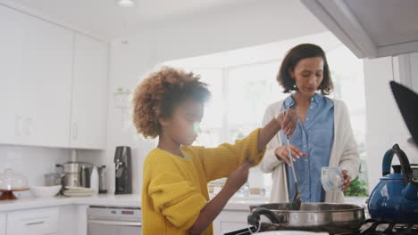 Pre-teen-African-American-girl-standing-at-hob-in-the-kitchen-preparing-food-with-her-mother,-low-angle-view