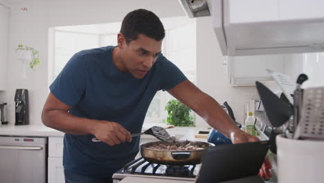 Hombre-Afroamericano-Milenario-Cocinando-En-La-Cocina,-Siguiendo-Una-Receta-En-Una-Tableta,-De-Cerca