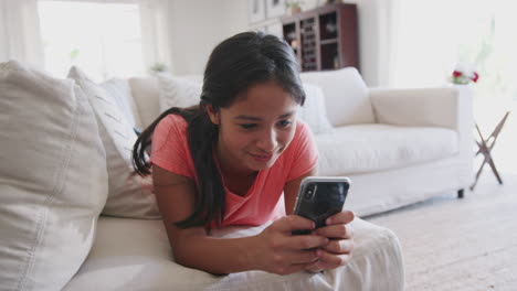 African-American-teenage-girl-lying-on-a-sofa-at-home-using-smartphone,-low-angle,-close-up