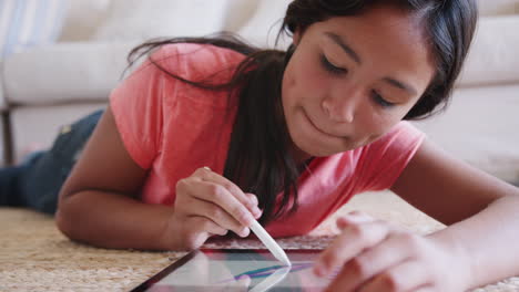 Teenager-Mädchen-Liegt-Im-Wohnzimmer-Auf-Dem-Boden-Und-Benutzt-Einen-Tablet-Computer-Und-Einen-Stift,-Nahaufnahme