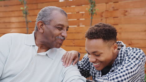 Senior-black-man-laughing-with-his-young-adult-grandson-outdoors,-close-up