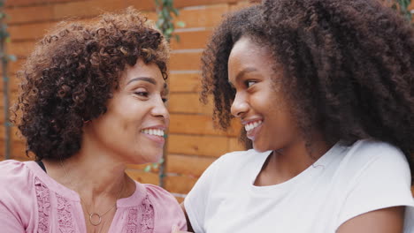 Middle-aged-black-mum-and-her-teenage-daughter-talking-and-smiling-at-each-other,-close-up