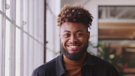 Millennial-black-male-creative-standing-in-office,-turning-and-smiling-to-camera,-close-up