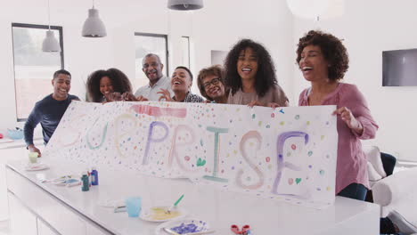 Three-generation-black-family-at-home-holding-up-a-sign-they’ve-made-for-a-surprise-party