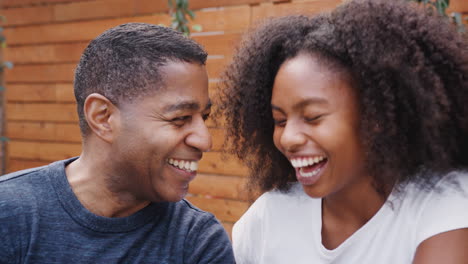Middle-aged-black-dad-and-his-teenage-daughter-talking-and-smiling-at-each-other-outdoors,-close-up