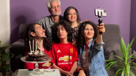 A-Persian-Iranian-family-party-birthday-ceremony-curly-hair-people-at-home-in-Tehran-Iran-Senior-man-closing-woman-eyes-for-surprise-Excited-mature-woman-looking-at-cake-with-burning-candles