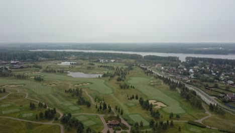 Toma-Aérea-De-Campos-De-Golf-Y-Municipio-Cerca-Del-Río