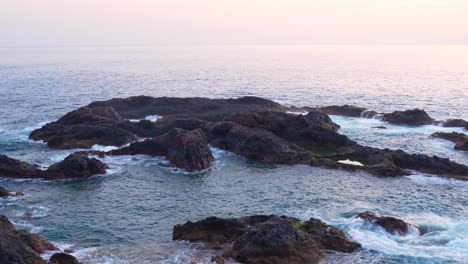 Soft-sunset-light-shines-on-rugged-rocks-as-waves-crash-in-slow-motion