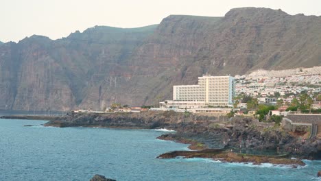 Resorts-and-hotels-at-the-seaside-of-Canary-Island-in-Tenerife-towards-the-sea,-handheld-tilting-upward
