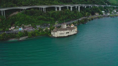 establish-shot-of-The-drone-camera-is-going-from-left-side-to-right-side,-rice-is-weaving-in-water-in-front-of-chillon-castle