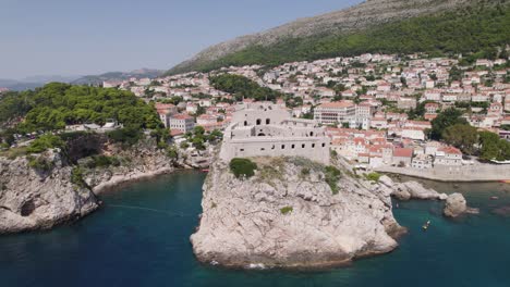 Rugged-cliffs-hold-up-Fort-Lovrijenac-in-Dubrovnik-Croatia,-aerial-pullback