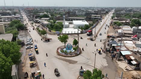 Vuelo-Aéreo-Sobre-La-Rotonda-De-Allaha-Wala-Chowk-Con-La-Mezquita-En-Segundo-Plano