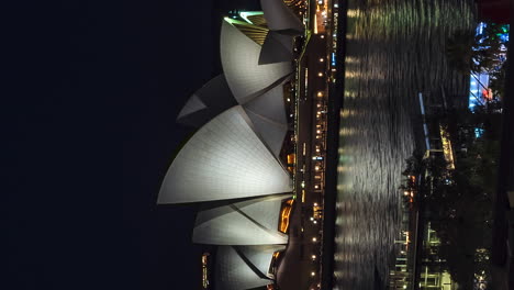 Vertical-timelapse-of-Sydney-Opera-House-at-night,-boats-sailing-in-harbor