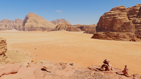 Push-in-to-cliff-edge-with-stacked-rocks-above-Wadi-Rum-desert