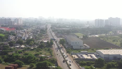 Rajkot-city-aerial-view-drone-camera-going-over-marutisuzuki-showroom,-big-truck-traffic-on-the-road
