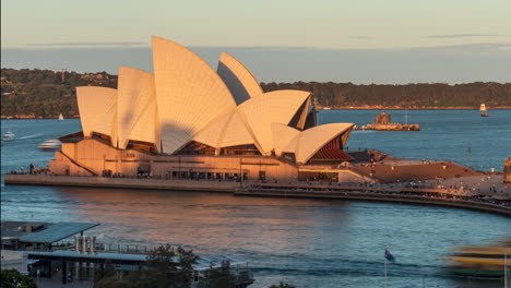 Menschen,-Die-Bei-Sonnenuntergang-Im-Opernhaus-Von-Sydney-Zu-Einer-Veranstaltung-Ankommen,-Zeitraffer-Von-Booten-Im-Hafen