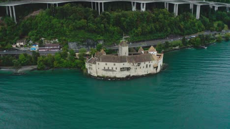 The-drone-camera-is-going-from-left-side-to-right-side,-rice-is-weaving-in-water-in-front-of-chillon-castle