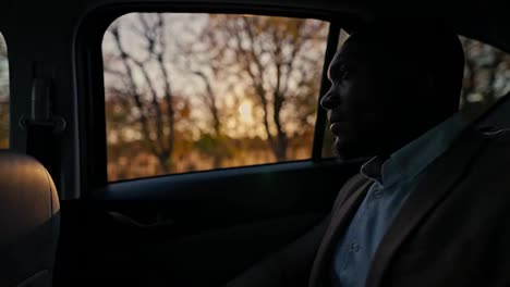 Side-view-of-a-male-businessman-with-Black-skin-with-a-beard-rides-in-a-car-during-his-business-trip-outside-an-urban-area-on-a-sunny-evening-at-sunset