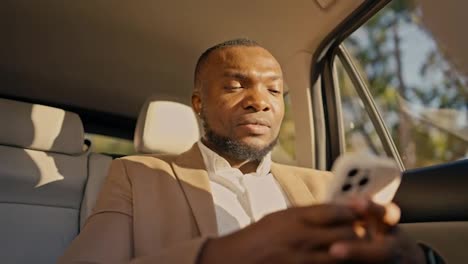 Confident-man-Businessman-with-Black-skin-color-in-a-brown-suit-drives-through-the-city-looking-out-the-window-and-chatting-on-his-white-phone-while-waiting-for-arrival