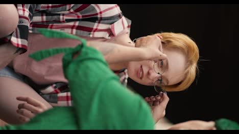 Vertical-video:-close-up-shot-of-a-girl-with-green-hair-taking-off-her-glasses-to-her-girlfriend,-a-blonde-with-a-short-haircut-wearing-a-checkered-pink-shirt-and-talking-to-her-on-her-date