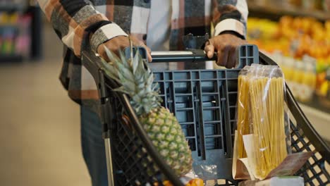 Close-up-shot-of-a-man-with-Black-skin-in-a-checkered-shirt-carrying-the-products-he-needs-into-a-cart-during-his-shopping-in-a-modern-grocery-store