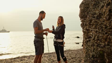 A-blonde-girl-with-curly-hair-in-black-clothes-teaches-her-brunette-boyfriend-in-a-gray-T-shirt-to-tie-special-knots-in-order-to-make-belay-while-folding