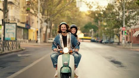 A-happy-guy-with-long-curly-hair-in-a-denim-jacket-rides-a-green-moped-with-his-brunette-girlfriend-in-a-plaid-shirt-who-shows-the-guy-with-her-index-finger-which-direction-they-should-go-along-a-city-street-in-the-summer