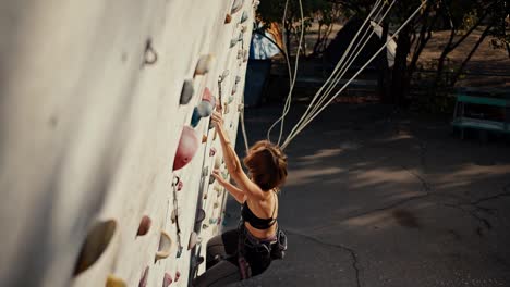 Top-view-of-a-blonde-girl-with-a-bob-hairstyle-in-a-black-top-and-black-pants.-She-climbs-a-special-structure-for-climbers-and-trains.-A-girl-in-climbing-gear-climbs-a-special-structure-for-climbing-training-during-the-day