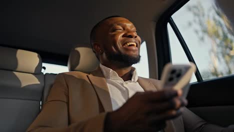 Happy-male-Businessman-with-Black-skin-and-a-beard-in-a-brown-suit-chatting-in-a-White-phone-and-driving-in-a-modern-car-along-the-city