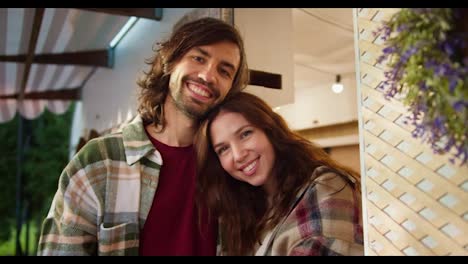 Portrait-of-a-happy-couple,-a-brunette-girl-in-a-plaid-shirt-puts-her-head-on-the-shoulder-of-a-brunette-guy-with-stubble-in-a-green-plaid-shirt-and-a-red-T-shirt-during-their-vacation-in-the-camp-near-a-trailer-near-a-picnic-outside-the-city-in-the-summer