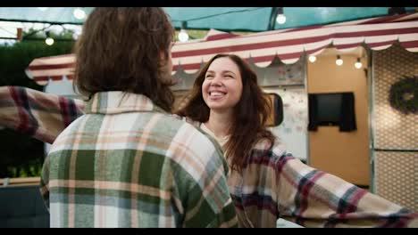 Happy-brunette-girl-in-a-pink-checkered-shirt-comes-out-of-her-trailer-and-hugs-her-brunette-boyfriend-in-a-green-checkered-shirt-during-her-vacation-outside-the-city-in-a-camp-during-a-picnic-in-the-summer