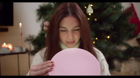 Una-Niña-Morena-Feliz-Abre-Una-Caja-Redonda-Rosa-Con-Su-Regalo-Y-Mira-Lo-Que-Hay-Dentro-Cerca-Del-árbol-De-Navidad-En-Una-Acogedora-Habitación-Decorada-En-Estilo-Navideño-Por-La-Noche.