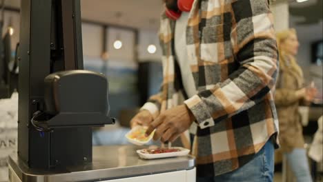 Close-up-shot-of-a-Black-man-in-a-checkered-shirt-scanning-the-goods-he-needs-at-a-self-service-checkout-in-a-modern-supermarket