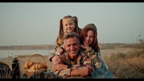 Trío-Familiar-Feliz:-Hombre-Moreno-De-Mediana-Edad,-Su-Esposa-Y-Su-Pequeña-Hija-Relajándose,-Divirtiéndose-Y-Posando-Durante-Sus-Vacaciones-En-Un-Picnic-Fuera-De-La-Ciudad-En-Verano