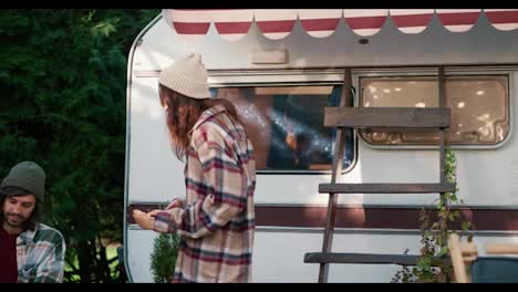 Una-Chica-Morena-Feliz-Con-Una-Camisa-A-Cuadros-Trae-Pasteles-Frescos-Para-Su-Novio-Moreno-Con-Una-Camisa-A-Cuadros-Verde.-Y-El-Chico-Sirve-Té-Caliente-En-Una-Taza-Y-Abraza-A-Su-Novia-Cerca-Del-Remolque-En-El-Campamento-Durante-Su-Picnic-Fuera-De-La-Ciudad-En-El-Verano.