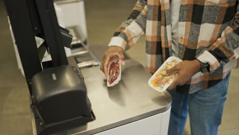 Close-up-shot-of-a-man-with-Black-skin-in-a-checkered-shirt-and-blue-jeans-scans-the-goods-he-needs-at-a-self-service-checkout-in-a-modern-large-grocery-store