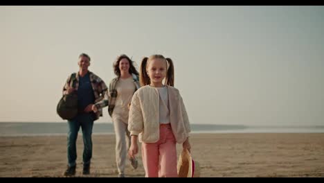 A-happy-little-blonde-girl-in-a-white-jacket-runs-along-the-path-and-her-parents-are-catching-up-with-her-from-behind.-And-the-brunette-man-with-gray-hair,-the-brunette-girl-in-a-checkered-green-shirt,-during-her-hike-and-picnic-outside-the-city