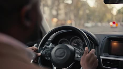 Over-his-shoulder-a-happy-male-businessman-with-Black-skin-color-in-a-brown-jacket-drives-a-modern-car-and-looks-at-the-road-during-his-business-trip-in-the-city