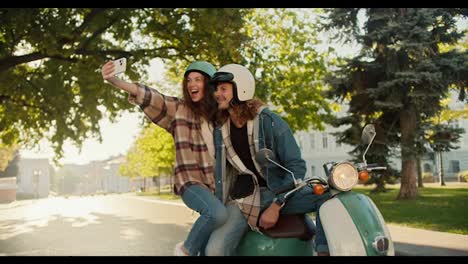 Happy-brunette-girl-in-a-checkered-shirt-and-jeans-takes-a-selfie-using-her-phone-with-her-boyfriend-who-is-sitting-on-a-moped-in-a-sunny-summer-city