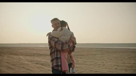 Zoom-in:-Portrait-of-a-little-blonde-girl-in-a-white-jacket-who-is-held-in-her-arms-by-her-father,-a-middle-aged-brunette-man-with-gray-hair-in-a-checkered-shirt-during-his-vacation-outside-the-city-in-the-summer-evening