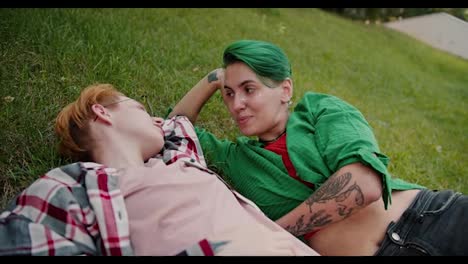 Two-lesbian-girls-with-short-bright-haircuts-in-plaid-shirts-lie-on-the-lawn-in-the-park-and-communicate-with-each-other-during-their-date