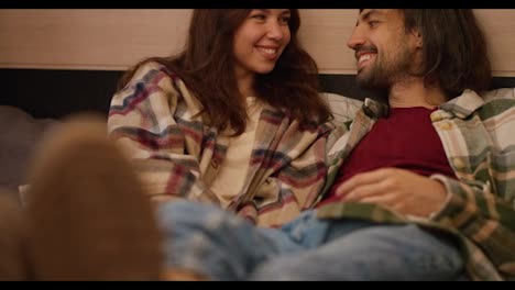 Close-up-shot-of-a-happy-couple,-a-brunette-girl-in-a-pink-plaid-shirt,-together-with-her-brunette-boyfriend-in-a-green-plaid-shirt,-lie-on-shoes-on-the-trailer-sofa-and-communicate-with-each-other-during-their-picnic-outside-the-city-in-a-camp-in-the-summer